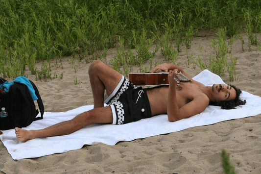 Image of man laying a on a oversized towel and playing guitar