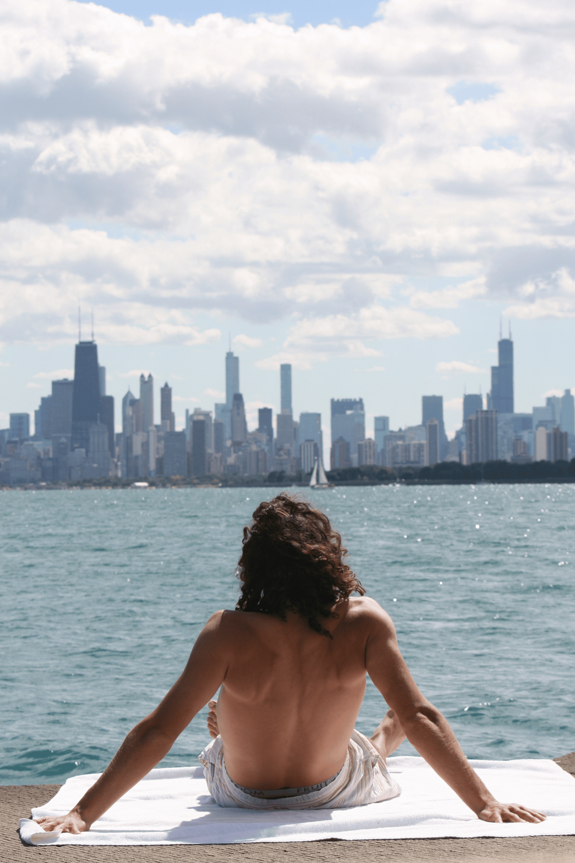 Person sitting on a oversized towel by the water with a city skyline in the background
