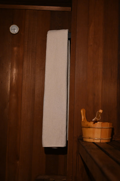 Giant white towel hanging in a sauna with a wooden bucket nearby.
